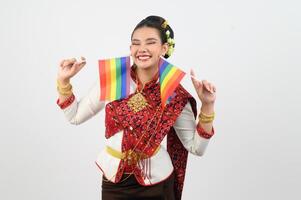 Porträt von jung Frau im thailändisch nordöstlich traditionell Kleidung halten Regenbogen Flagge foto