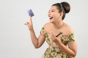 junge asiatische schöne braut, die in der hand mit kreditkarte und schönheitspinsel postet foto