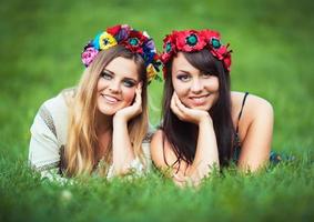 zwei Lachen Mädchen im ukrainisch National Kostüme Lüge auf das Grün Gras foto