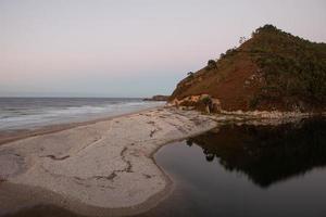 Strand mit Bergen im Hintergrund und warmem Sonnenuntergangslicht foto