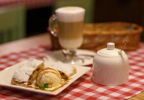 Kaffee Latté im Glas Tasse und und Strudel mit Eis Sahne auf ein Tischdecke im ein Käfig foto