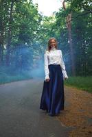 Frau im ein schön Outfit Spaziergänge durch das Wald, umhüllt im Blau Rauch foto