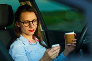 Geschäftsfrau Senden ein Text Botschaft und Trinken Kaffee während Fahren ein Auto foto