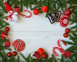 Weihnachten Rand mit Tanne Baum Geäst, Weihnachten Dekorationen und Süßigkeiten Stock auf Weiß hölzern Bretter foto