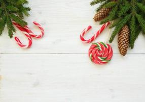 Weihnachten Rand mit Tanne Baum Geäst mit Zapfen und Süßigkeiten Stock auf Weiß hölzern Bretter foto