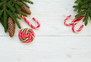 Weihnachten Rand mit Tanne Baum Geäst mit Zapfen und Süßigkeiten Stock auf Weiß hölzern Bretter bereit foto