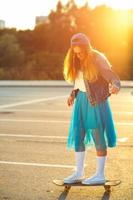 draussen Mode Nahansicht Sommer- Porträt von ziemlich jung Frau posieren mit Skateboard im städtisch Jugend Stil im Stadt. Sommer- Abend Sonnenlicht foto