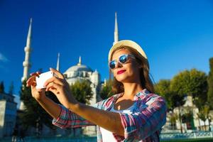 Mädchen im das Hut Herstellung Selfie durch das Smartphone auf das Hintergrund von das Blau Moschee, Istanbul foto