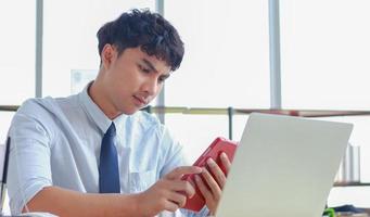junger asiatischer Geschäftsmann, der mit einem Laptop in einem modernen Büro arbeitet