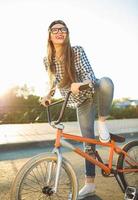 schön jung Frau im ein Hut Reiten ein Fahrrad auf Stadt Hintergrund im das Sonnenlicht draussen foto
