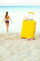 Gelb Koffer auf das Strand und ein Mädchen Spaziergänge in das Meer im das Hintergrund foto
