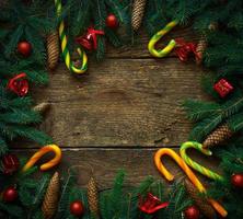 Weihnachtsgrenze mit Tannenzweigen, Zapfen, Weihnachtsschmuck und Zuckerstange auf rustikalen Holzbrettern foto