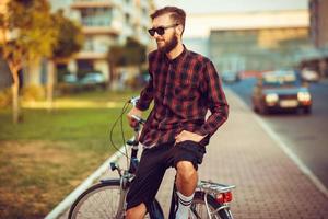 Mann im Sonnenbrille Reiten ein Fahrrad auf Stadt Straße foto