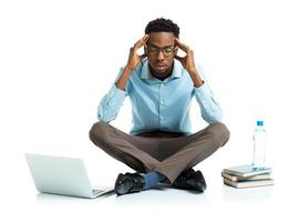 afrikanisch amerikanisch Hochschule Schüler im Stress Sitzung mit Laptop, Bücher und Flasche von Wasser auf Weiß foto