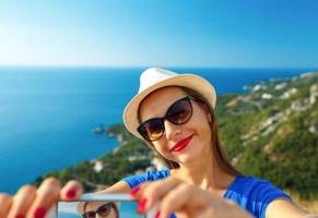 Mädchen im das Hut Herstellung Selfie durch das Smartphone auf das Hintergrund von Meer Küste, adriatic Meer foto