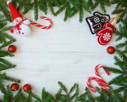 Weihnachten Rand mit Tanne Baum Geäst, Weihnachten Dekorationen und Süßigkeiten Stock auf Weiß hölzern Bretter foto