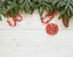 Weihnachten Rand mit Tanne Baum Geäst mit Zapfen und Süßigkeiten Stock auf Weiß hölzern Bretter foto