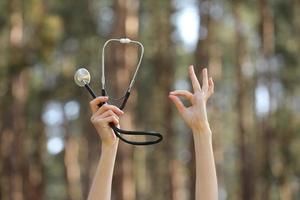 Hände halten ein Stethoskop und zeigen okay Zeichen auf Natur Wald Hintergrund foto