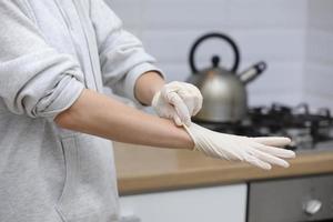 jung Frau Putten auf schützend Handschuhe auf Hände während Arbeiten von Zuhause oder beim das Büro Arbeit durch das Tabelle Laptop im Tag verhindern Virus Verbreitung während Epidemie im Quarantäne. selektiv Fokus foto