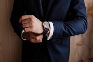 Geschäftsmann, der die Zeit auf seiner Armbanduhr überprüft, Mann, der die Uhr auf die Hand legt, Bräutigam, der sich morgens vor der Hochzeitszeremonie fertig macht. Mann legt eine Uhr an. selektiver Fokus foto