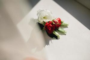 Nahansicht das Bräutigam Knopfloch Weiß und rot Blumen und Grün und Grün Lügen auf das Tisch. Braut Vorbereitungen. Hochzeit Morgen Konzept foto