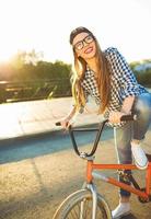 schön jung Frau im ein Hut Reiten ein Fahrrad auf Stadt Hintergrund im das Sonnenlicht draussen foto