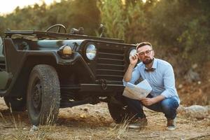 jung stilvoll Mann mit Brille und Bogen Krawatte sehen das Karte in der Nähe von das altmodisch suv foto