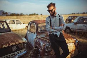 jung gut aussehend stilvoll Mann, tragen Hemd und Krawatte auf das Feld von alt Autos foto