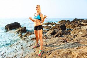 Athlet Frau tun Sport ausüben mit das Seil auf das Felsen durch das Meer foto