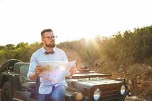 jung stilvoll Mann mit Brille und Bogen Krawatte sehen das Karte in der Nähe von das altmodisch suv foto