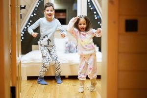 Kinder im Sanft warm Pyjama spielen beim hölzern Kabine heim. Konzept von Kindheit, Freizeit Aktivität, Glück. Bruder und Schwester haben Spaß und spielen zusammen. foto