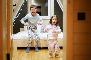 Kinder im Sanft warm Pyjama spielen beim hölzern Kabine heim. Konzept von Kindheit, Freizeit Aktivität, Glück. Bruder und Schwester haben Spaß und spielen zusammen. foto