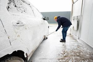 Mann wäscht amerikanisches SUV-Auto mit Wischmopp in einer Selbstbedienungswäsche bei kaltem Wetter. foto