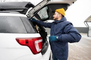 mann wischt kofferraum eines amerikanischen suv-autos mit einem mikrofasertuch ab, nachdem er sich bei kaltem wetter gewaschen hat. foto