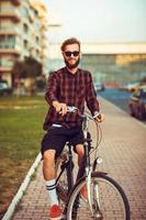 stilvoll Mann im Sonnenbrille Reiten ein Fahrrad auf Stadt Straße foto