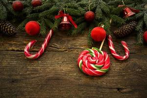 Weihnachtsgrenze mit Tannenzweigen, Zapfen, Weihnachtsschmuck und Zuckerstange auf rustikalen Holzbrettern foto