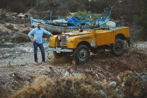 jung stilvoll Mann mit Brille und Bogen Krawatte in der Nähe von das altmodisch suv foto