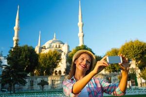 Mädchen im das Hut Herstellung Selfie durch das Smartphone auf das Hintergrund von das Blau Moschee, Istanbul foto