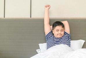 fettleibig Fett Junge wacht auf oben und Dehnen auf Bett im Morgen, foto