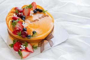 Orange Kuchen mit glücklich Geburt Tag und gekrönt mit orange, Erdbeere, Blaubeere foto
