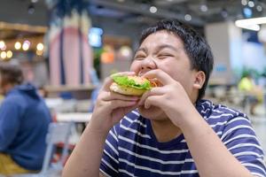 fettleibig Junge isst ein Hamburger im ein Essen Gericht im ein Einkaufen Center. Müll Essen foto