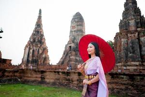 schön thailändisch Mädchen im traditionell Kleid Kostüm rot Regenschirm wie thailändisch Tempel wo ist das Öffentlichkeit Ort, thailändisch Frau im traditionell Kostüm von Thailand. foto