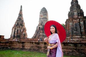 schön thailändisch Mädchen im traditionell Kleid Kostüm rot Regenschirm wie thailändisch Tempel wo ist das Öffentlichkeit Ort, thailändisch Frau im traditionell Kostüm von Thailand. foto