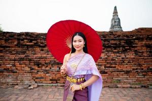 schön thailändisch Mädchen im traditionell Kleid Kostüm rot Regenschirm wie thailändisch Tempel wo ist das Öffentlichkeit Ort, thailändisch Frau im traditionell Kostüm von Thailand. foto