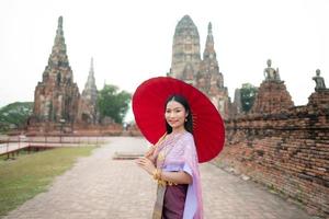 schön thailändisch Mädchen im traditionell Kleid Kostüm rot Regenschirm wie thailändisch Tempel wo ist das Öffentlichkeit Ort, thailändisch Frau im traditionell Kostüm von Thailand. foto