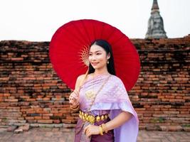 schön thailändisch Mädchen im traditionell Kleid Kostüm rot Regenschirm wie thailändisch Tempel wo ist das Öffentlichkeit Ort, thailändisch Frau im traditionell Kostüm von Thailand. foto