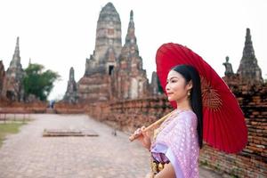 schön thailändisch Mädchen im traditionell Kleid Kostüm rot Regenschirm wie thailändisch Tempel wo ist das Öffentlichkeit Ort, thailändisch Frau im traditionell Kostüm von Thailand. foto