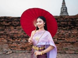 schön thailändisch Mädchen im traditionell Kleid Kostüm rot Regenschirm wie thailändisch Tempel wo ist das Öffentlichkeit Ort, thailändisch Frau im traditionell Kostüm von Thailand. foto