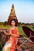 schön thailändisch Mädchen im traditionell Kleid Kostüm rot Regenschirm wie thailändisch Tempel wo ist das Öffentlichkeit Ort, thailändisch Frau im traditionell Kostüm von Thailand. foto