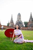 schön thailändisch Mädchen im traditionell Kleid Kostüm rot Regenschirm wie thailändisch Tempel wo ist das Öffentlichkeit Ort, thailändisch Frau im traditionell Kostüm von Thailand. foto